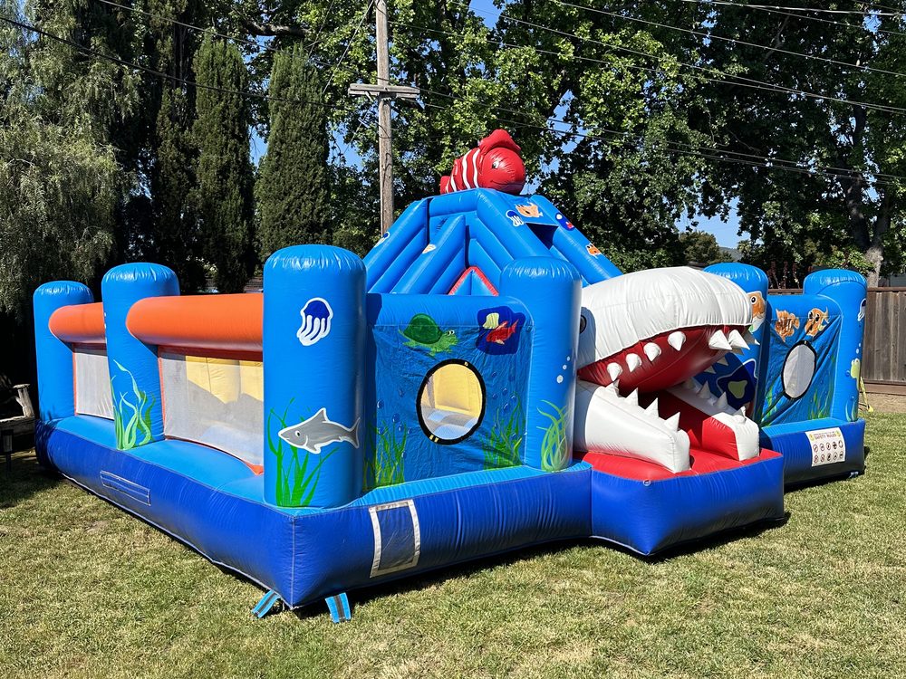Ocean themed inflatable combo with a shark tunnel, slide and open play area on grass