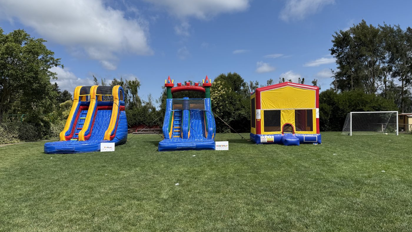 Three inflatables lined up on a school field: a tall waterslide, a slide combo and a standard bounce house, with grade level signs in front