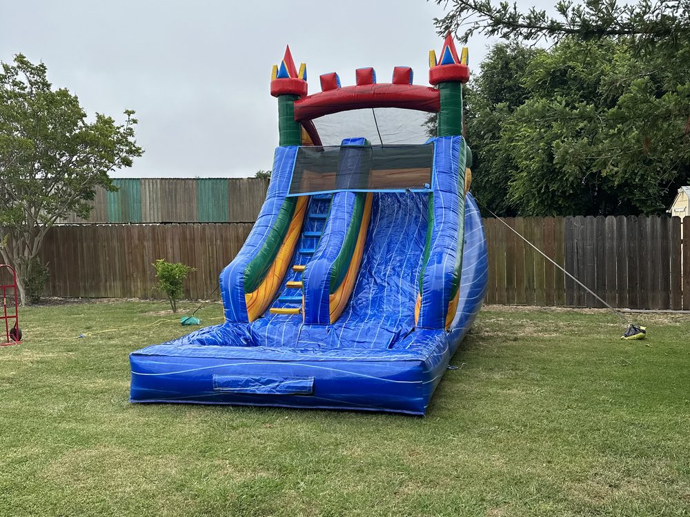 Blue and green inflatable waterslide with a splash pool, set up on a grass lawn